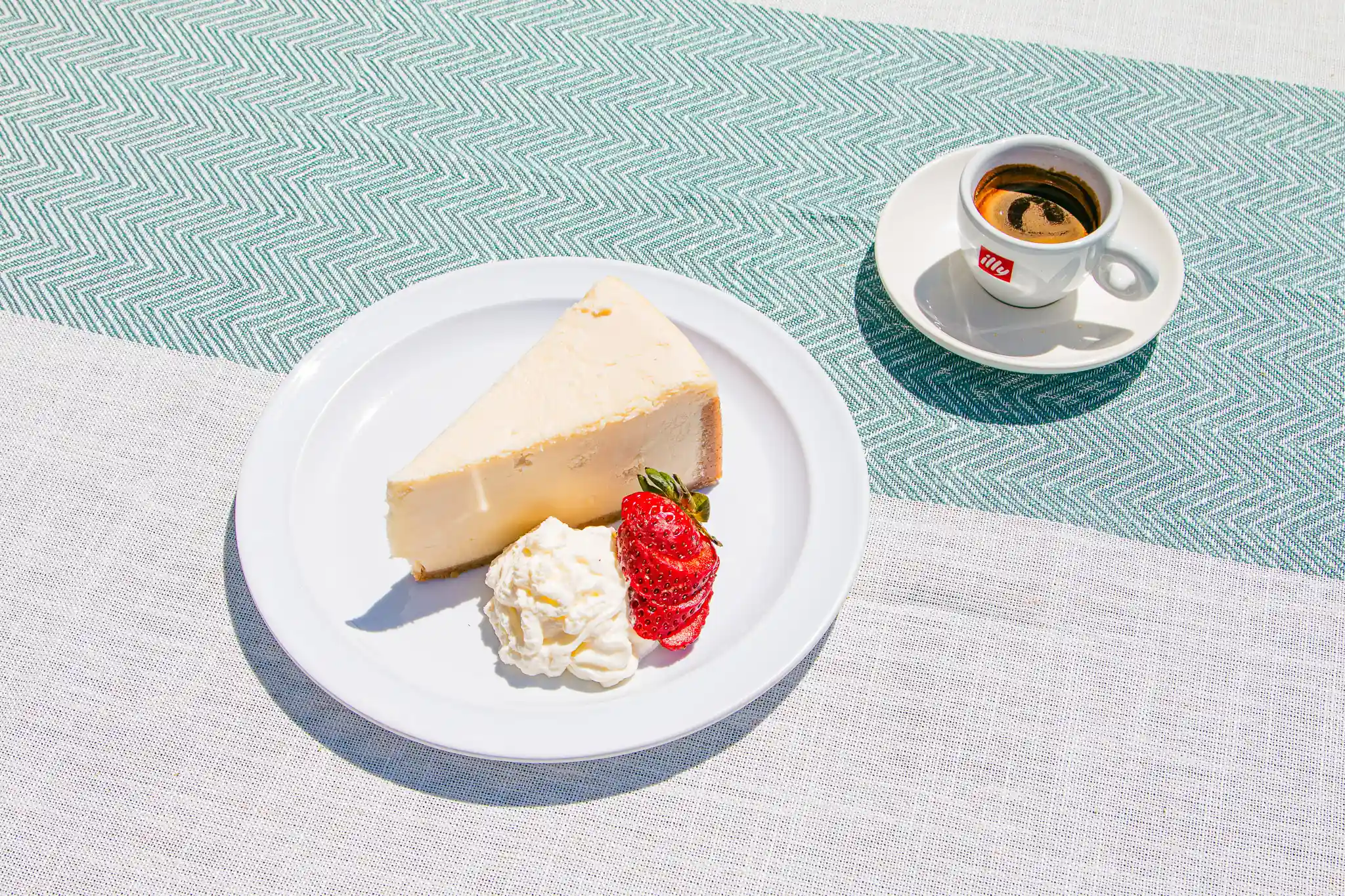 Cheesecake with cream and a strawberry beside an espresso