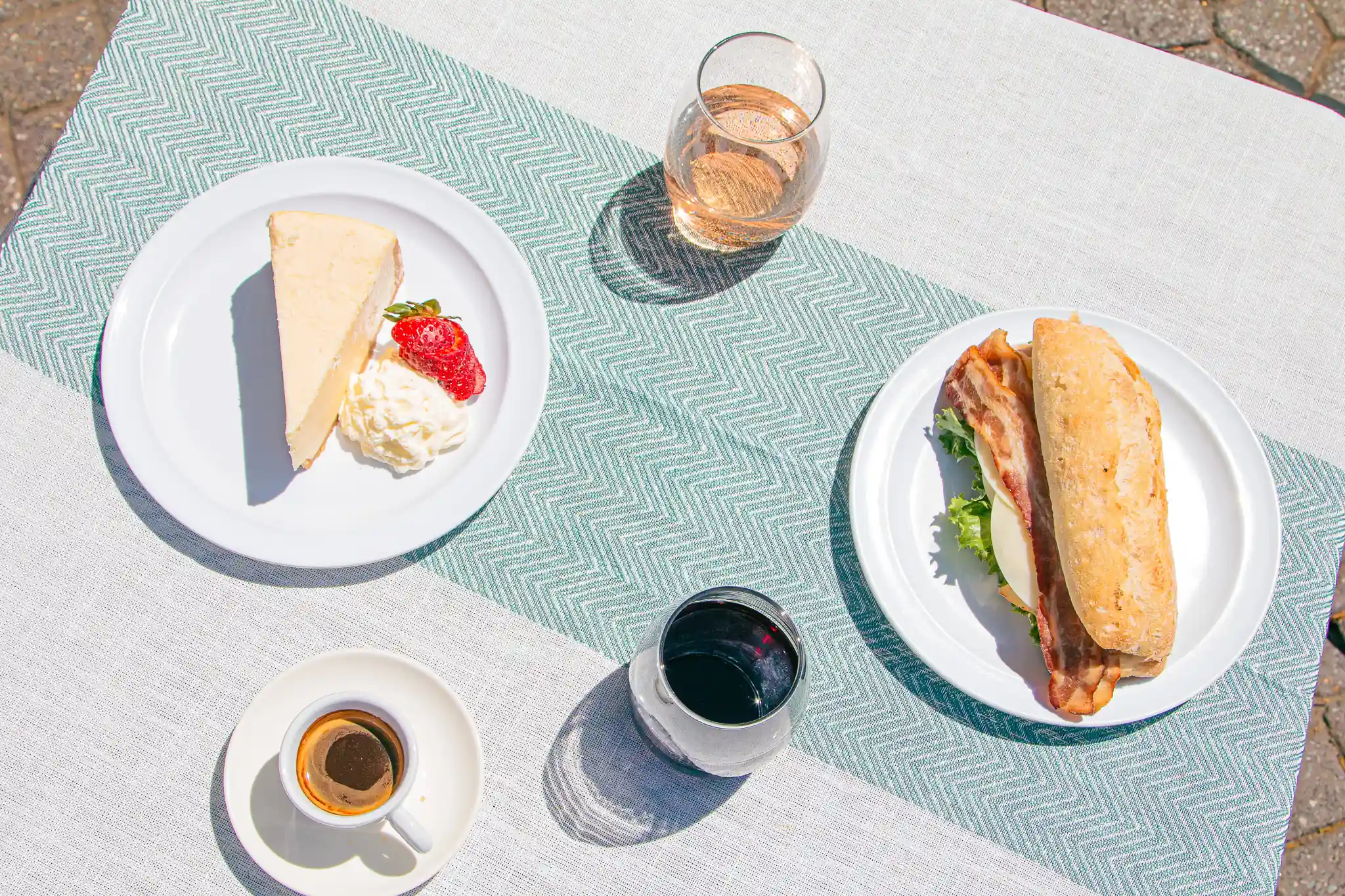 Cheesecake, a sandwich, espresso and wine on teal linen, seen from above