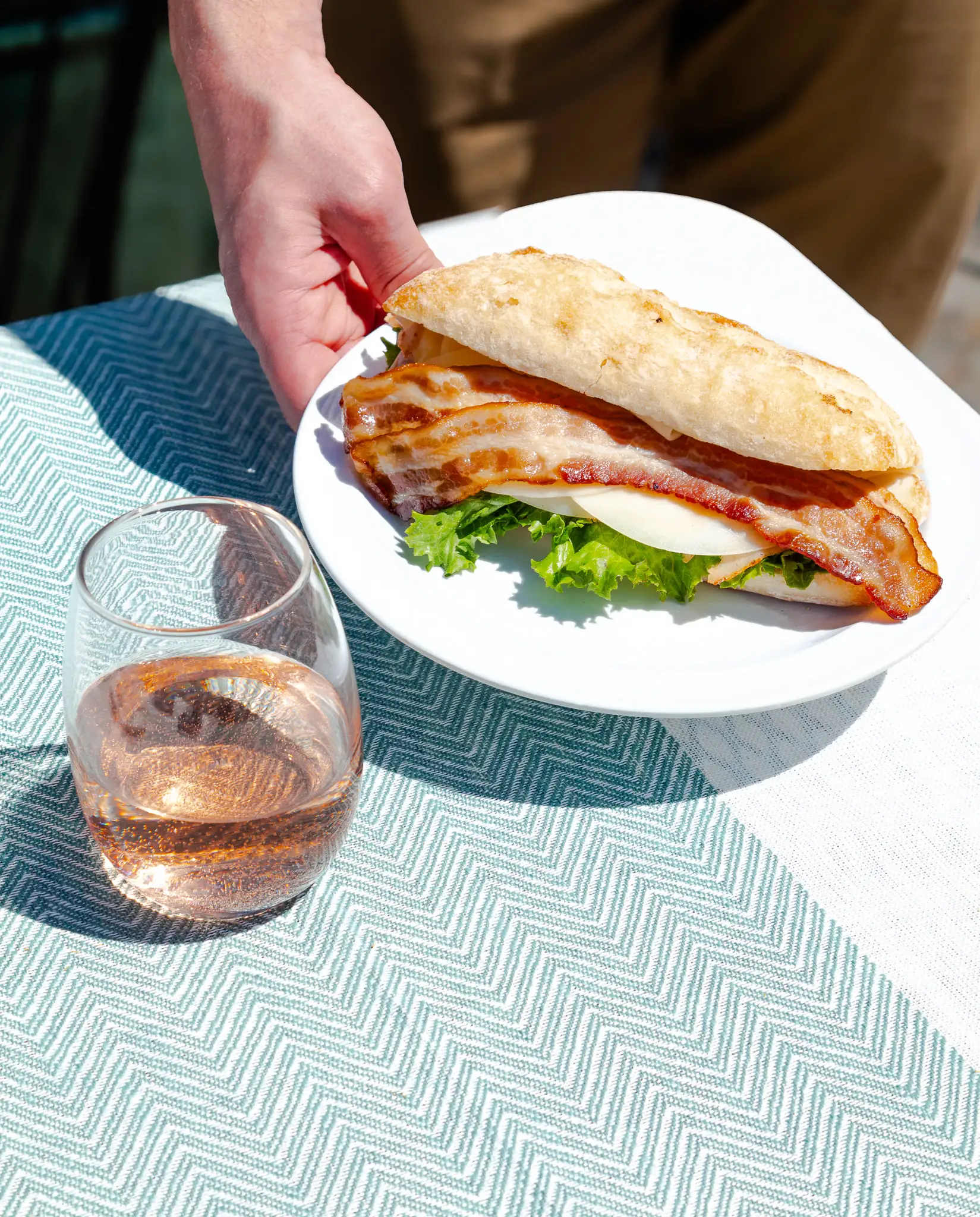 A sandwich and a glass of rosé set down on the patio table